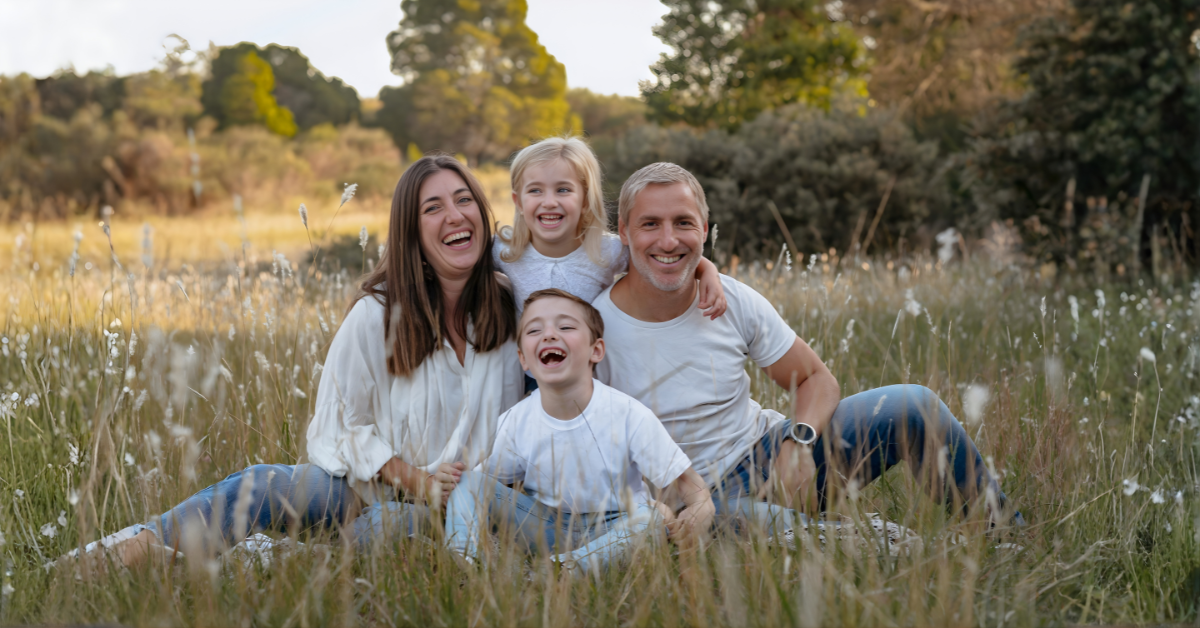 Smiling family sitting together outdoors during summer vacation, symbolizing peaceful co-parenting and quality time.