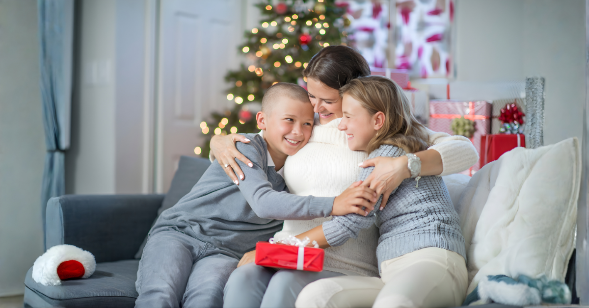 Mother hugging her two children on the couch during a warm holiday celebration with a Christmas tree.