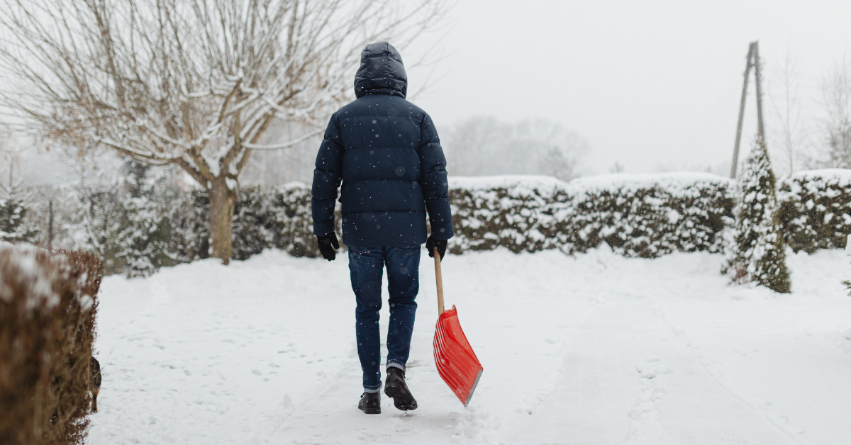 A person walking alone through a snowy yard holding a red shovel, symbolizing navigating the holidays without your children.
